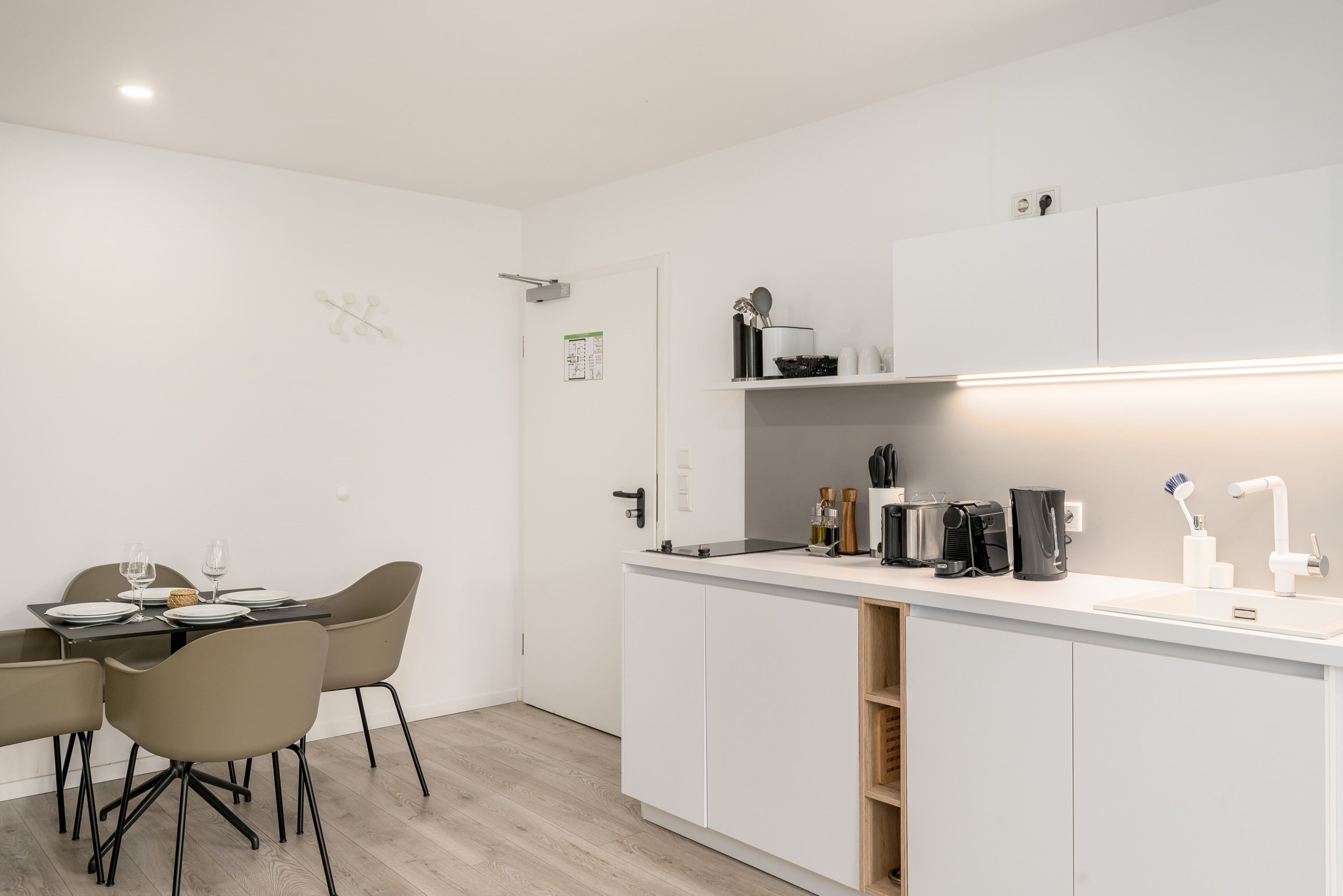 A modern kitchen with white cabinets, a dining table with chairs, and a coffee machine.
