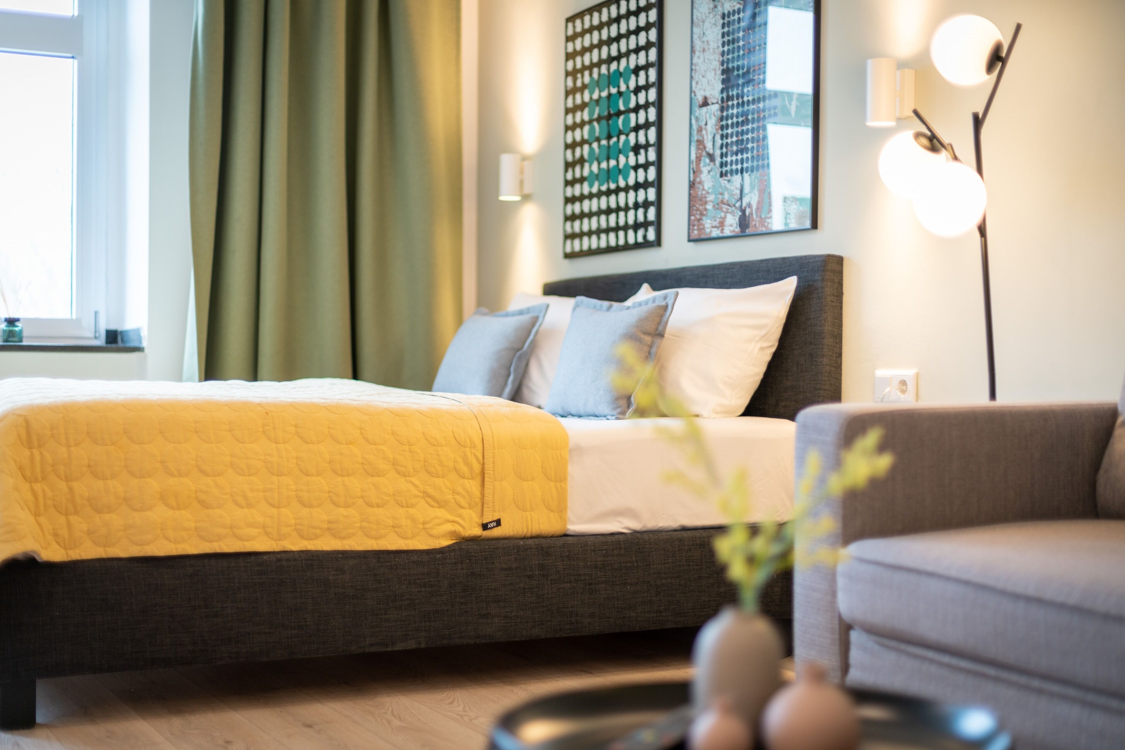 A modern bedroom with a bed, a grey sofa, and a floor lamp.