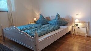 Un lit simple avec un cadre blanc, une literie bleue à motifs et des oreillers assortis. Deux lampes de chevet sont posées sur des tables de chevet blanches.