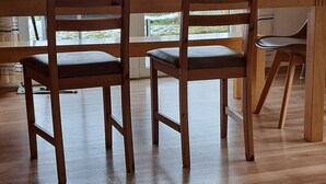 Un espace repas comprenant une table et des chaises en bois, un luminaire en fibres tressées et de grandes fenêtres offrant une vue dégagée.