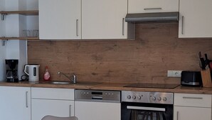 Une cuisine moderne avec des armoires blanches, un plan de travail en bois, un four encastré et un coin repas comprenant une table et un banc en bois.