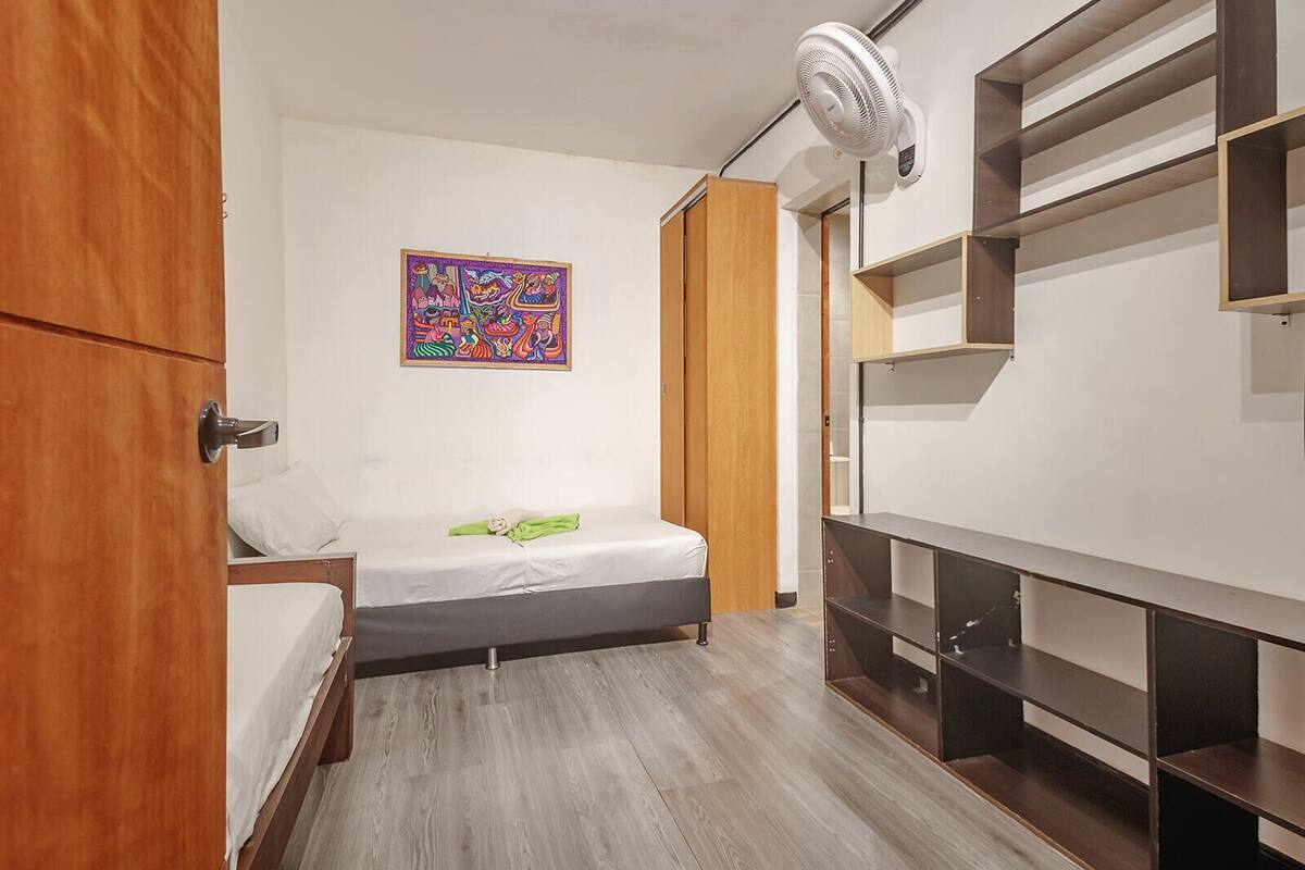 Un dormitorio pequeño y moderno con cama, armario de madera, estante en la pared y una obra de arte colorida.