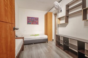 Ein kleines, modernes Schlafzimmer mit einem Bett, einem Holzschrank, einer an der Wand befestigten Ablage und einem farbenfrohen Kunstwerk.