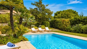 A swimming pool with lounge chairs and a towel, surrounded by greenery and trees.