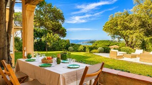 An outdoor dining area with a table set for four, overlooking a well-manicured garden and a view of the sea.