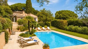 Una piscina con lettini, una scala che conduce a un edificio e una vegetazione curata.