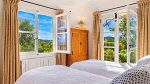 A bedroom with two beds, a wooden wardrobe, and large windows with curtains.