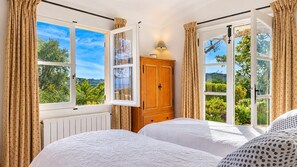 A bedroom with two beds, a wooden wardrobe, and large windows with curtains.