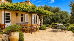 A patio with a wooden table and chairs, surrounded by potted plants and a stone floor.