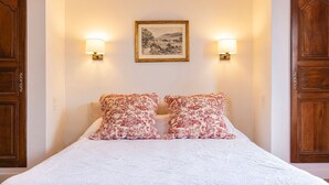 Un letto con due cuscini floreali, un quadro raffigurante un paesaggio sopra e due lampade a parete su entrambi i lati.