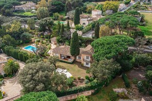 A large house with a swimming pool, surrounded by lush greenery and trees.