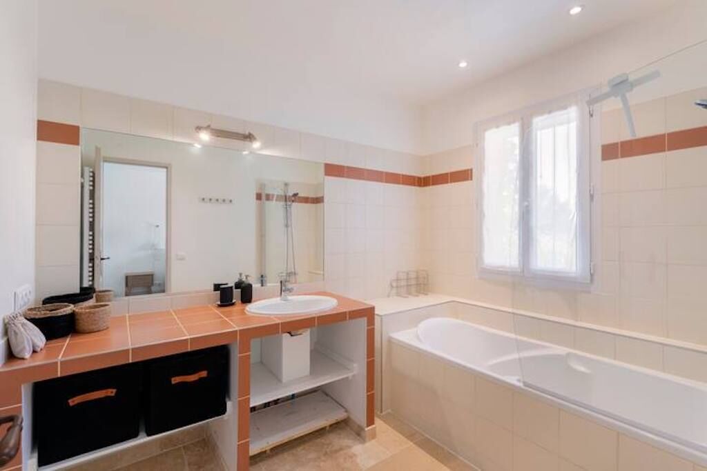 A modern bathroom with a large mirror, two sinks, a bathtub, and a window.