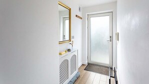 En smal hall med en vit dörr, en glasdörr, en spegel med en guldfärgad ram och ett litet konsolbord.