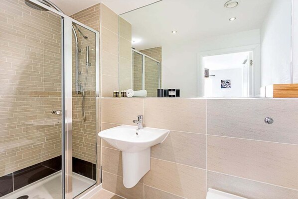 A modern bathroom with a glass-enclosed shower, a white pedestal sink, and beige tiled walls.