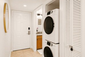 A laundry room with two stacked front-loading washing machines, a white door, and a mirror on the wall.