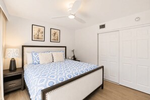 A bedroom with a bed, nightstand, lamp, ceiling fan, and two framed pictures on the wall. - Park Shore Resort 2nd Floor BLDG J #254 (Park Shore Resort)