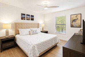 A bedroom with a bed, bedside tables, a ceiling fan, a window with blinds, and wall art.