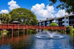 A red bridge over water with a fountain, surrounded by greenery and buildings. - Park Shore Resort 2nd Floor BLDG J #254 (Park Shore Resort)