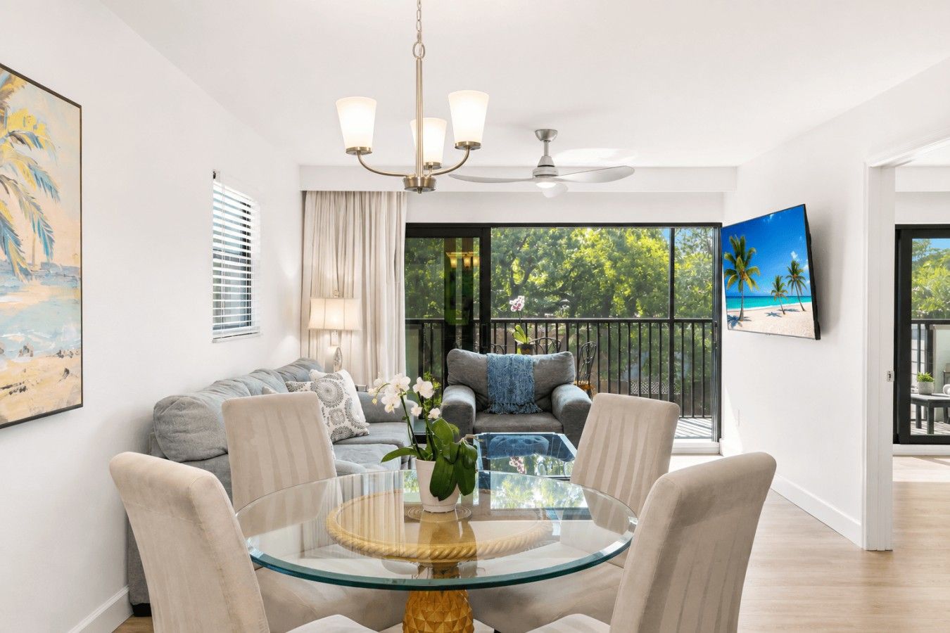 A modern living room with a glass dining table, a sofa, and a ceiling fan.