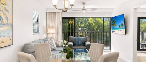 A modern living room with a glass dining table, a sofa, and a ceiling fan.