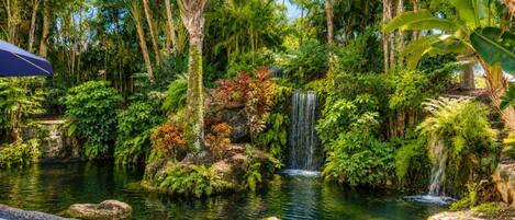 A tranquil garden with a pond, a waterfall, and lush vegetation.