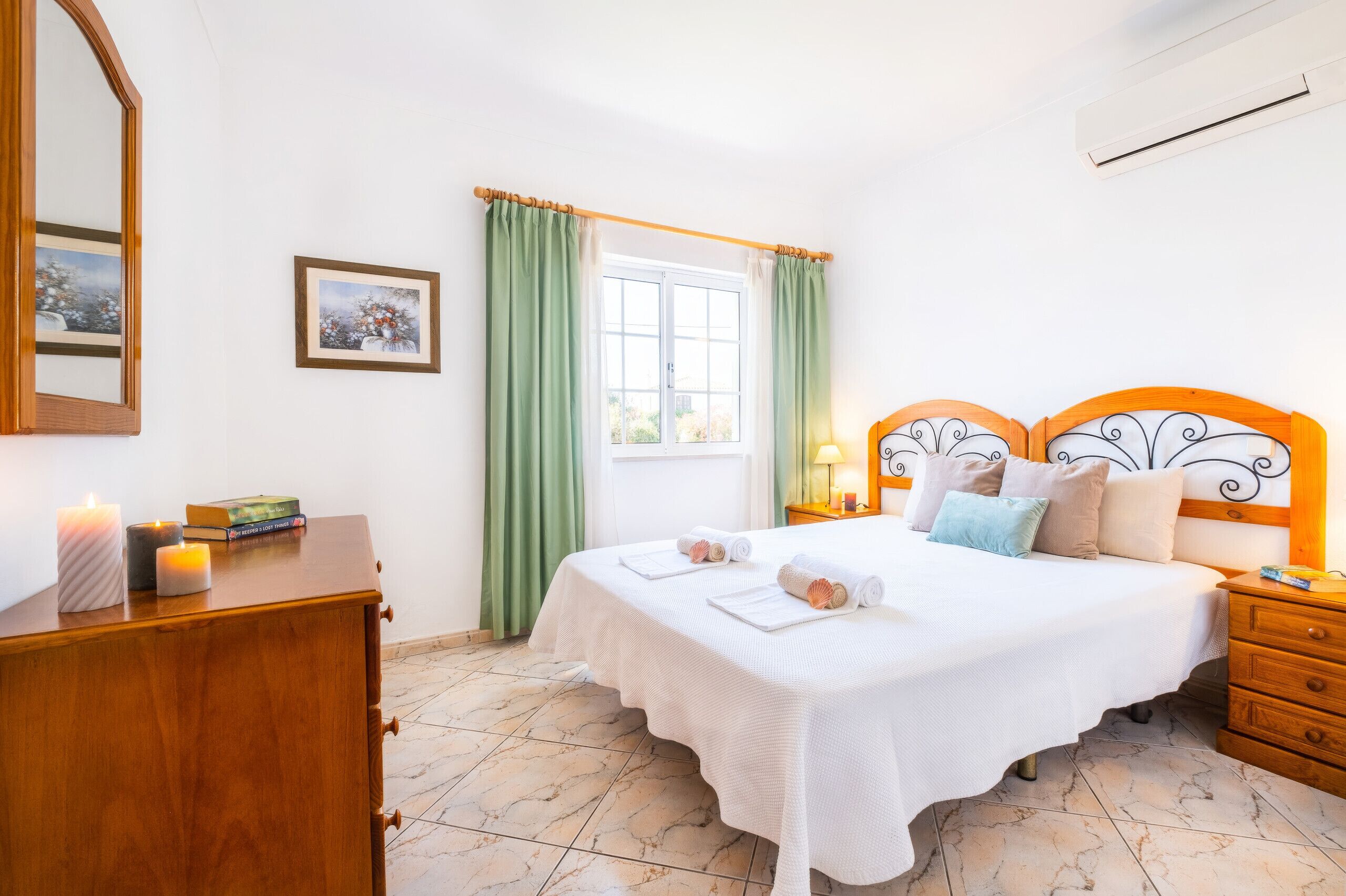 Un dormitorio con cama, cómoda, espejo, ventana con cortinas, un cuadro en la pared y un equipo de aire acondicionado.