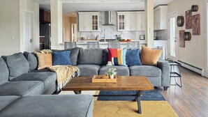 A modern living room with a gray sectional sofa, a wooden coffee table, and a kitchen in the background. - Mountain Paradise - Pickleball / Hot Tub / Games (Jewett)