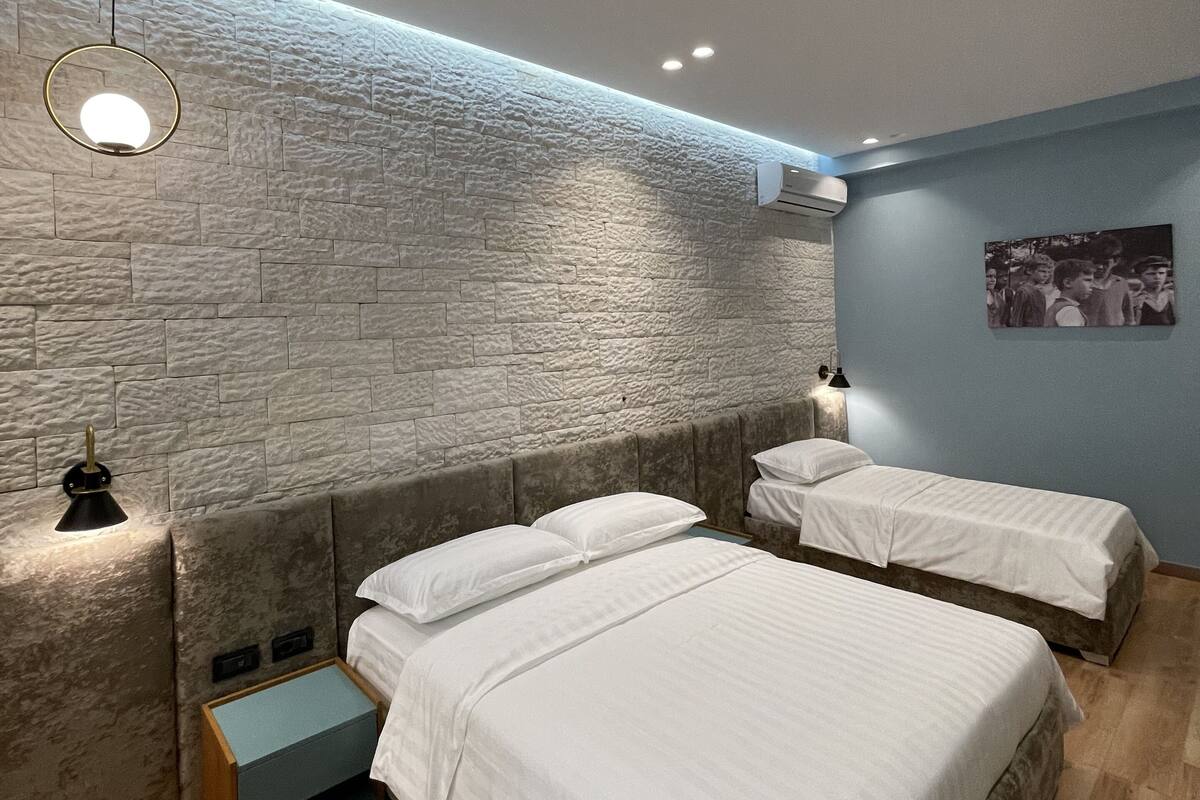 A modern bedroom with two beds, a stone-textured wall, and a blue accent wall.
