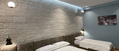 A modern bedroom with two beds, a stone-textured wall, and a blue accent wall.
