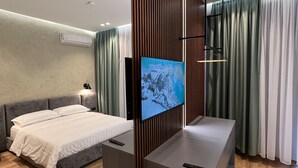 A modern hotel room with a large bed, a TV mounted on a wooden panel, a small desk, and a seating area with a sofa. - Bujtina Apsus (Berat)