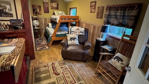 Ein gemütliches Zimmer mit einem Etagenbett, einem Ledersessel, einem Schreibtisch mit Computer und einem Teppich mit historischen Mustern.