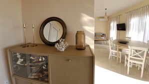 Een eetruimte met een ronde tafel en stoelen, een aan de muur bevestigde televisie, en een decoratieve vaas op een kast.
