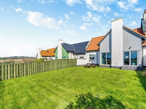 A modern house with a well-maintained lawn, a wooden fence, and a picnic table.