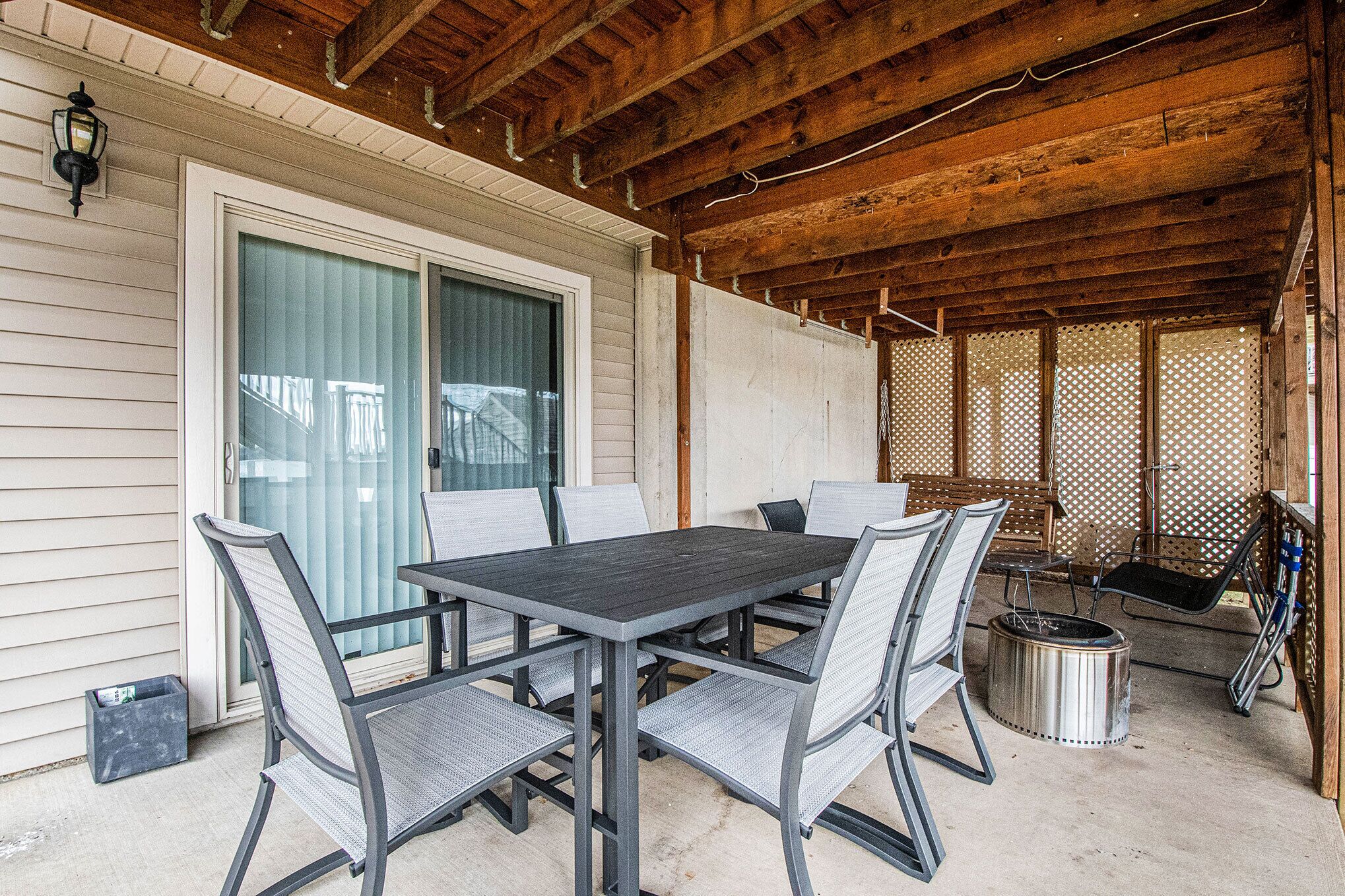 Une terrasse couverte avec une table et des chaises, une poubelle en métal et un plafond en bois.