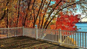 A wooden deck with a white railing overlooking a body of water, surrounded by trees with autumn foliage.