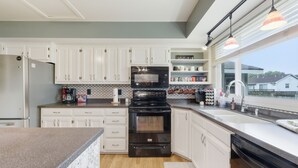 A modern kitchen with white cabinets, a black stove, and a large window providing a view of the outside. - Hot Tub - Pool Table - Fire Pit - Family Friendly!  Hosted by Homes by CNJ. (Wichita)