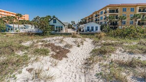 A beachfront property with a sandy path leading to a row of houses, featuring balconies and a clear blue sky. - Private cottage | 50 steps to BEACH! (Indian Rocks Beach)