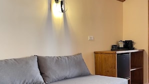 A cozy room with a grey sofa, a wooden table, and a small kitchenette area with a coffee maker and kettle. - Midgard Suites - Medieval Town (Rhodes)