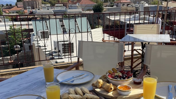 A terrace with a table set for breakfast, including croissants, pastries, and fruit, overlooking a historic cityscape with a prominent tower. - Midgard Suites - Medieval Town (Rhodes)