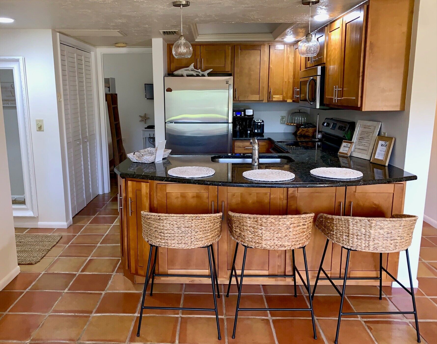 A kitchen with a central island, wooden cabinets, a stainless steel refrigerator, and a large TV.
