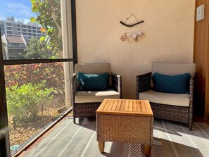 A balcony with wicker furniture, a small table, and a view of buildings and trees. - Midnight cove II 414F: Ground-Floor Condo with Beach, Pool, and Tennis! (Siesta Key)