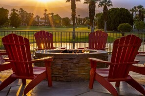 A fire pit with four red Adirondack chairs around it, set on a patio with a view of a golf course and palm trees in the background. - COACHELLA Marriott's Desert Springs Villas  (Palm Desert)