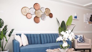 A blue sofa, a wooden coffee table, and a beige armchair in a living room with a wall-mounted decorative piece and a potted plant. - Modern Paradise Island Condo near Atlantis resort & beach (Nassau)