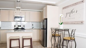 A modern kitchen with a central island, stainless steel appliances, and a dining area with metal chairs. - Modern Paradise Island Condo near Atlantis resort & beach (Nassau)