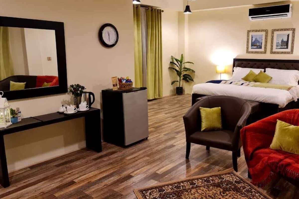 A hotel room with a bed, a desk, a chair, a sofa, a mirror, a clock, and a plant.