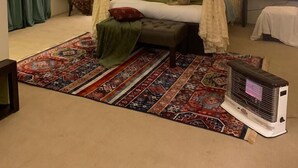 A bedroom with a four-poster bed, a patterned rug, a heater, and a chair with a red cushion. - The Mandarin Inn (Gilgit)