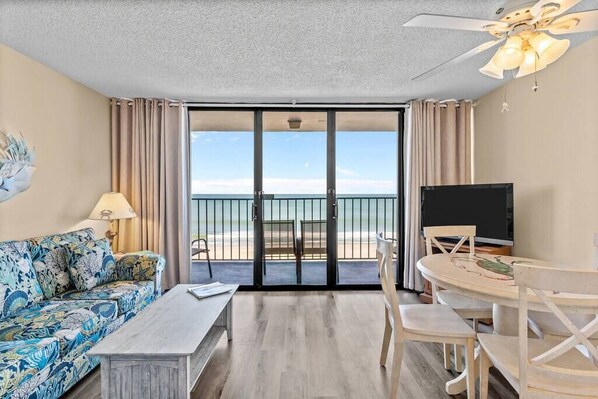Habitación con sofá, mesa, televisión y balcón con vistas a la playa.