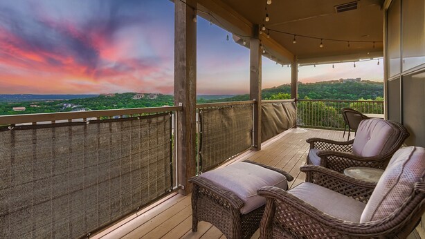 A balcony with wicker furniture and a view of a sunset over a cityscape. - Lake View @ Hollows Resort: Pools, Pets, Balconies (Jonestown)