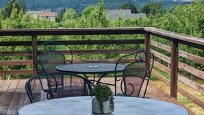 Una terraza de madera con una mesa redonda y sillas, con vistas a un paisaje montañoso con picos nevados.