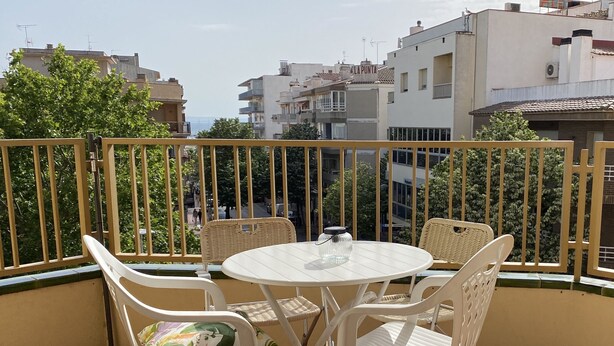 Een balkon met een ronde tafel en vier stoelen, omgeven door een gele balustrade.